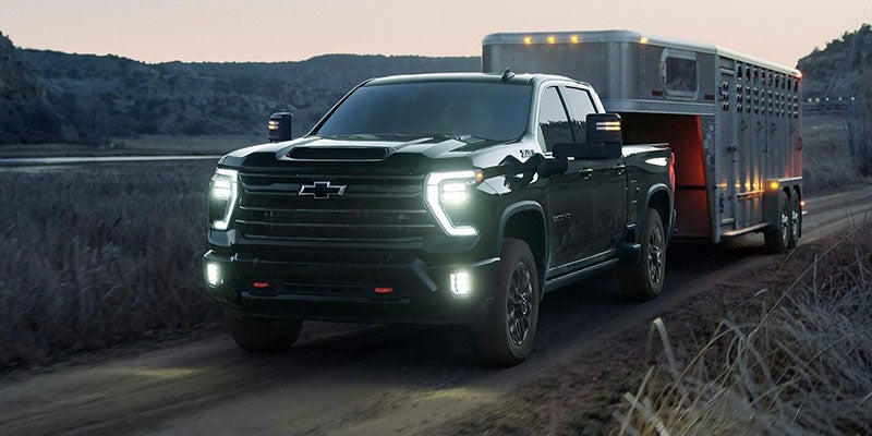 A Chevrolet Silverado towing a large trailer on a highway, showcasing its robust design and towing capability.
